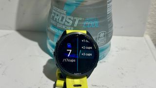 A Garmin Forerunner 965, showing the hydration tracking data app, sits in front of a bottle of Gatorade.